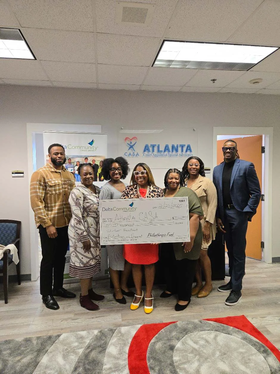 Eight people stand in the Atlanta CASA office holding a large Delta Community Credit Union check made out to Atlanta CASA