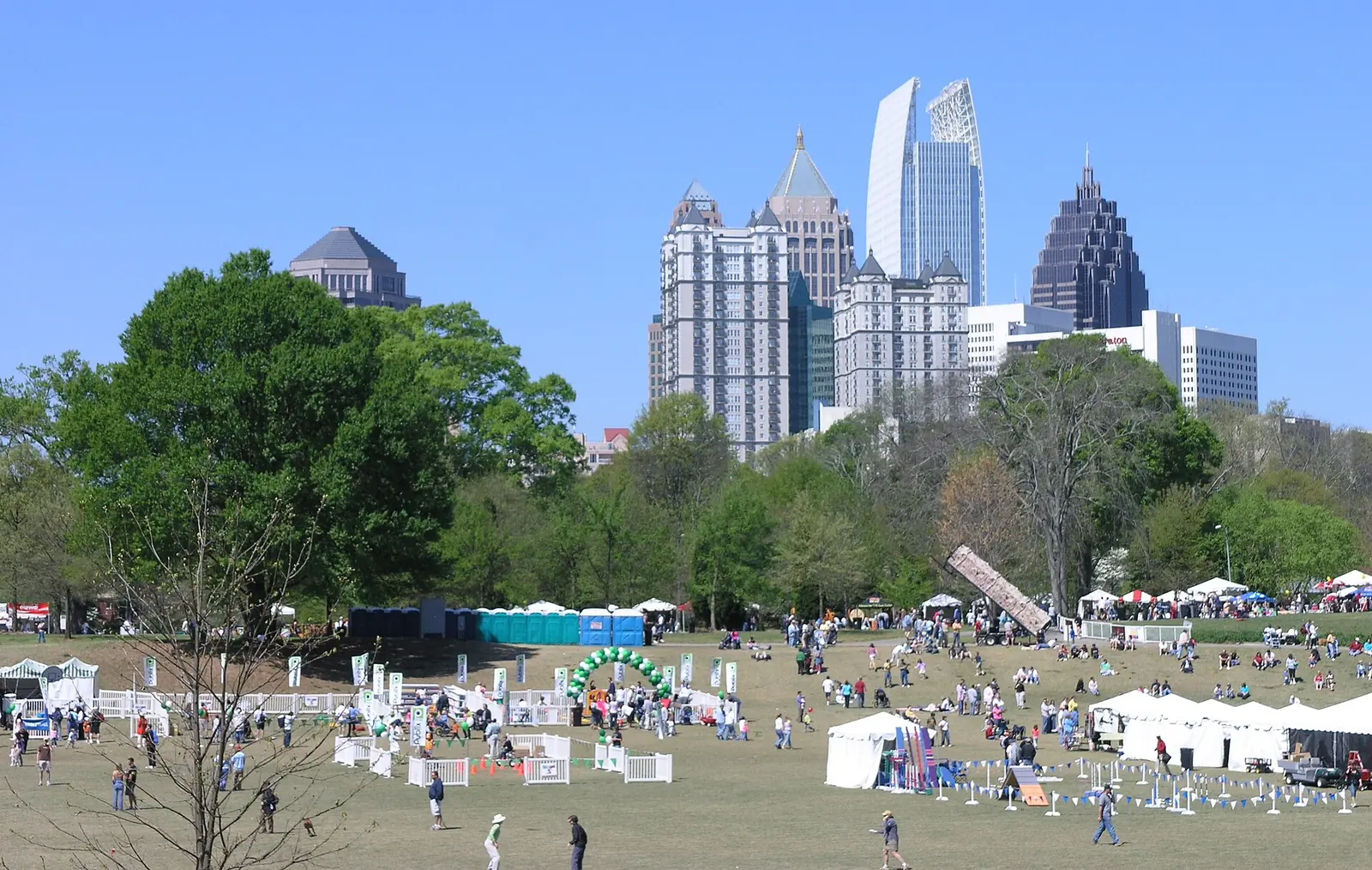 Crowds on the meadow at Piedmont Park during a festival, with the Midtown skyline behind.